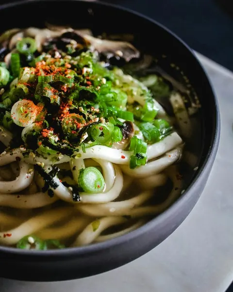 검은 그릇에 담긴 칼국수 위에 파와 김가루, 고춧가루가 올라 있다